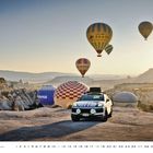 Porsche Cayenne, Kalender mit Tagen 1-31. Auto vor felsiger Landschaft, bunte Heißluftballons im Morgenlicht.