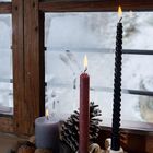 Drei brennende Kerzen auf einem Fensterbrett, umgeben von Walnüssen, getrockneten Orangenscheiben und einem Tannenzapfen.