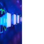 Links "34", rechts "35". Blau-grüne Neonbeleuchtung entlang einer Wand mit runden und quadratischen Elementen.