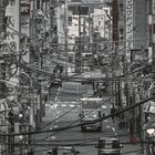 Viele Schilder mit japanischen Schriftzeichen, überladen mit Stromkabeln, belebte Straße mit Autos und Fußgängern.