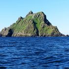 Keine Texte vorhanden. Eine felsige Insel mit grüner Vegetation ragt aus dem blauen Ozean unter einem klaren Himmel.