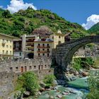 "Viele Legenden ranken sich um die alte Römerbrücke, die Pont-Saint-Martin, die den Fluss Lys überpannt." Steinbrücke und Gebäude.