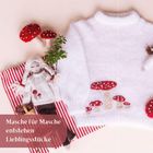 „Masche für Masche entstehen Lieblingsstücke”. Ein weißer Pullover mit Pilzmotiven, Stoffpuppe und rote Streifenunterlage.