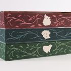 Drei Buchrücken mit geschnörkeltem Muster in Rot, Blau, Grün und Tiergesichtern in der Mitte der Ranken.