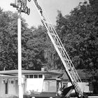 Ein Mann auf einem hohen, scherenartigen Kran repariert Scheinwerfer an einem Mast neben einem Kleintransporter.