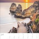 Kalenderseite für Juli. Foto zeigt Holztreppe zu Strand mit Felsen im Meer bei Sonnenuntergang.