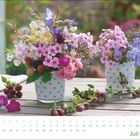 Kalender für Juli mit bunten Sommerblumen in gepunkteten Töpfen auf einem Holztisch.
