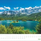 Kalenderblatt mit Juli-Kalender. Landschaftsaufnahme: Ein See mit grünen Inseln vor einer Bergkulisse unter blauem Himmel.