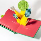 Ein Popup-Buch mit roten Seiten zeigt geometrische Formen und Texte wie: "Ein bunter Strauß aus magischen Bildern!"