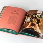 Text links: "Zur Ruhe kommen". Rechts hält jemand eine Tasse, vor einem Tablett mit asiatischem Essen.