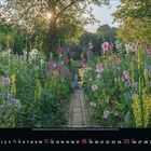 Monatskalender: Juli. Bunter Blumengarten im Sonnenlicht mit einem schmalen Pfad, der zu einem alten Torbogen führt.