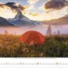 7, Juli. Eine orange Zelt auf einer Wiese, umgeben von Bergen bei Sonnenaufgang mit leichtem Nebel.