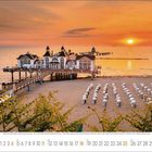 Text unten: Zahlen von 7 bis 31, darunter Wochentage.  
Motiv: Steg ins Meer bei Sonnenuntergang und zahlreiche Strandkörbe am Strand.