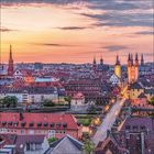 Es gibt keine Texte im Bild. Eine Stadtansicht bei Sonnenuntergang, Brücke führt in die Altstadt mit Kirchtürmen und beleuchteten Straßen.