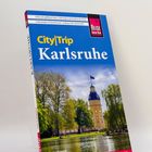 Reiseführer "City|Trip Karlsruhe" mit Schloss und Bäumen. Autornamen "Günter Schenk" und Hinweis auf City-Faltplan.