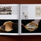 "CARTIER SANTOS" oben, "1915" rechts. Offenes Buch zeigt Fotos von Uhren, historische und technische Skizzen.