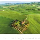 7, Kalenderansicht. Eine Hütte auf einem Hügel, umgeben von Feldern und Bäumen in einer grünen Landschaft.