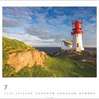 Juli, Kalenderansicht: Ein Leuchtturm auf einem grasbewachsenen Felsen, Blick auf das Meer, teils bewölkter Himmel.