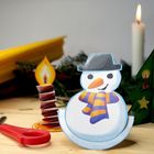 Ein Schneemann mit Hut und Schal, Kerze, Tannenbaum mit Kerzen und Kugeln. Zu sehen sind Schere und Bastelmaterial.