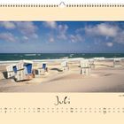 Kalendereintrag Juli mit Strandkörben am Sandstrand vor der Küste. Wolkenloser Himmel, ruhige See, aufgeräumte Atmosphäre.