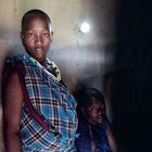 Keine sichtbaren Texte. Zwei Personen in traditioneller, bunter Kleidung in einem dunklen Raum, beleuchtet von einem kleinen Licht an der Wand.