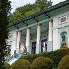 Ein prächtiges Gebäude mit weißen Säulen, verziert mit blauen und goldenen Akzenten, umgeben von viel Grün.