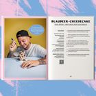 Text: BLAUBEER-CHEESECAKE ohne Boden, aber umso mehr Geschmack. Junger Mann mit Cap und Tattoos isst Kuchen.
