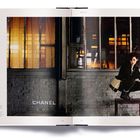 Links Text: "CHANEL". Rechts Frau auf einem Hocker vor einem Backsteinfenster in dunkler Kleidung, orangefarbene Beleuchtung.