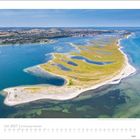 Juli 2027 | Schleswig-Holstein. Luftaufnahme von einer Landzunge mit grünen und sandigen Flächen umgeben von blauem Wasser.
