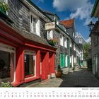"galerie rouge", Kalender für Juli 2027. Kopfsteinpflasterstraße mit historischen Fachwerkhäusern und bunter Fassade.