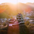 Keine Texte zu sehen. 

Eine japanische Burg vor einer Hügelkulisse bei Sonnenuntergang.