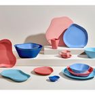 Geschirr in Blau und Rosa auf weißen Stufen, asymmetrische Formen, Tassen, Schalen und Teller sind sichtbar.