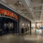 Text: "Legändärer Zufallsfund: Der Schriftzug 'Powerhouse' zierte Mitte der 1990er Jahre das Eingangsportal des wichtigsten Hip-Hop-Clubs Hamburgs. Im Rahmen der Recherche für die Ausstellung trieb das Kuratorenteam die originalen aus Blech geformten roten Buchstaben auf. Sie hatten jahrzehntelang in einer Scheune vor den Toren Hamburgs herumgestanden."  
Logo: "POWERHOUSE" in großen, roten Buchstaben.  
Beschreibung: Ein Museum mit Ausstellungsstücken, Kleidungsstücken und Wandbildern.