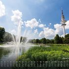 "Planten un Blomen" unten rechts. Kalenderdaten unten. Springbrunnen in einem Park mit Turm und blauem Himmel.