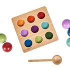 Quadratische Holzplatte mit farbigen Löchern, daneben bunte Holzkugeln und ein Holzlöffel.