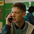 Zu sehen ist eine Person mit Telefon. Im Hintergrund ein "PAYPOINT"-Schild und eine zweite Person bei Waschmaschinen.