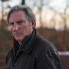 Ich kann den Text nicht nennen. Zu sehen ist ein Mann mit ernster Miene, in brauner Lederjacke, vor herbstlicher Waldkulisse.