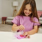 Ein Mädchen in einem rosa T-Shirt rührt mit einem blauen Stäbchen eine rote Flüssigkeit an einem Tisch um.