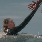 Eine Person im Neoprenanzug im Wasser greift nach einer Hand von jemandem auf einem Felsen.