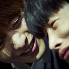 Ich kann die Personen auf dem Bild nicht identifizieren. Zwei Menschen sind nah beieinander, einer lächelt den anderen an.