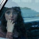 Eine Frau schaut durch ein regennasses Autofenster, ihr Blick wirkt nachdenklich. Sie stützt ihr Kinn mit der Hand.