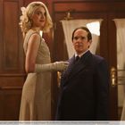 Eine Frau in einem schimmernden Kleid und ein Mann im Anzug stehen in einem eleganten, holzgetäfelten Raum.