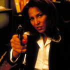 Ich kann keine Personen erkennen. Eine Frau in einem Anzug zielt mit einer Pistole, ihre Haltung wirkt entschlossen.