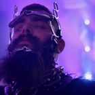 Ich sehe keine Texte. Ein bärtiger Mann mit Metallgestell im Gesicht vor lila Scheinwerfern.