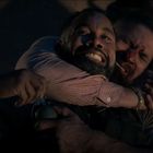 Zwei Männer ringen miteinander; einer hält den anderen von hinten im Würgegriff. Sie wirken angespannt und kämpferisch.