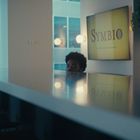 „SYMBIO“ auf einem Bildschirm. Ein Mann schaut knapp über einer glänzenden Theke hervor. Moderne Küche mit Pflanzen.