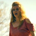 Ich kenne keine Texte in diesem Bild. Eine Frau mit langem blondem Haar und erschrockener Miene, trägt ein rotes Oberteil.