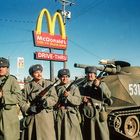 McDonald's Logo und Schilder "OVER 45 BILLION SERVED" und "DRIVE-THRU", dazu vier Soldaten in Winteruniformen vor einem Panzer.