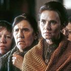 Vier ernst schauende Frauen eng beieinander, eine trägt ein braunes, grobmaschiges Tuch.