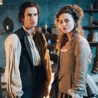 Zwei Personen in historischer Kleidung stehen in einem rustikalen, altmodischen Raum mit Regalen und Kupfergeschirr.